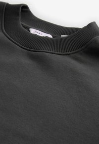 Sudadera de cuello redondo en gris oscuro con cuello ribeteado, textura suave y un brillo sutil. Presenta una etiqueta en el cuello.
