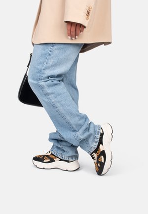 Zwart en bruin sneakers met een luipaardprint ontwerp, dikke witte zool, gecombineerd met lichtblauwe denim jeans en een beige blazer.