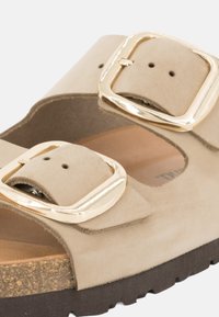 Sandal in suede beige con due fasce larghe dotate di grandi fibbie in tono oro, sottopiede in sughero e suola in gomma testurizzata.