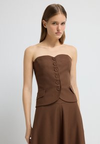 Hnědý top bez ramínek s texturovanou látkou, se siluetou přiléhající k tělu, šesti knoflíkovými zapínáními a dvěma bočními kapsami.