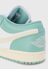 Gros plan sur le talon d'une chaussure Air Jordan turquoise et blanche avec logo de basketball ailé et semelle rainurée sur fond clair.