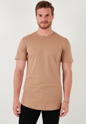 Camiseta de manga corta en color tostado, hecha de un material suave y con un cuello redondo. Presenta un corte regular y un detalle de etiqueta en el lado inferior izquierdo.