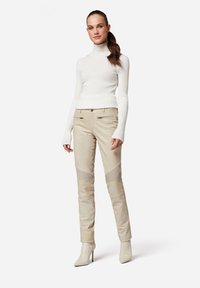 Weiße gerippte Rollkragenpullover kombiniert mit beigen schmalen Hosen mit Mesh-Details und glänzender Oberfläche, abgerundet mit cremefarbenen High-Heels.