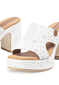 Sandalias de plataforma blancas con patrones florales cortados a láser, tacón alto en forma cónica, puntera abierta y plantilla de madera natural.