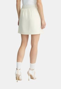 Una gonna A-line color crema con una fascia elastica in vita. Indossata con tacchi trasparenti e calzini bianchi, che mettono in mostra linee pulite e un design minimal.