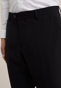 Svarta skräddarsydda byxor i slätt tyg med platt fram, bälteshällor och knappstängning i midjan. Det finns detaljer på fickkanterna.