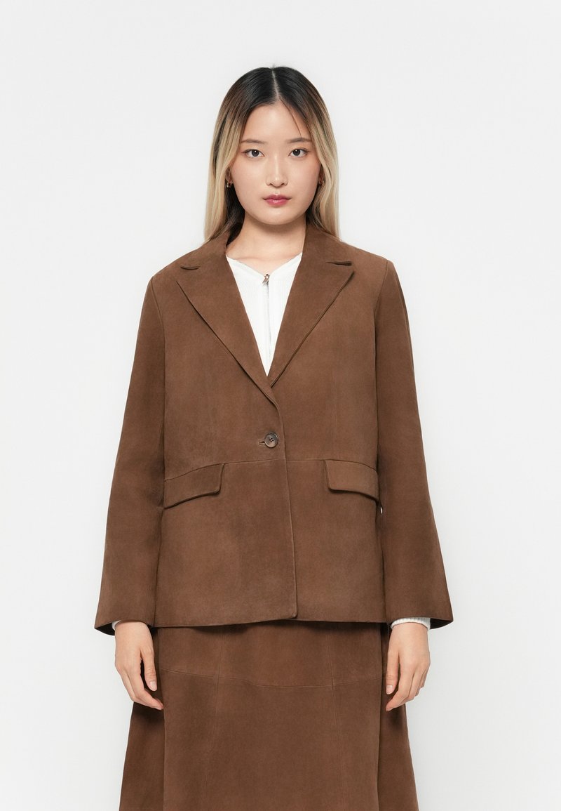 Blazer en daim brun avec une fermeture à un bouton, des revers crantés et deux poches avant. Texture lisse et coupe décontractée avec des manches évasées.