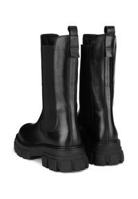 Czarne skórzane buty z elastycznymi panelami po bokach i masywną czarną gumową podeszwą. Projekt zawiera pętelki z tyłu ułatwiające zakładanie.
