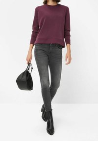 Sweat-shirt bordeaux, jean skinny gris et bottines noires. Tenant un sac noir. Design simple et texture lisse sur l'ensemble de la tenue.
