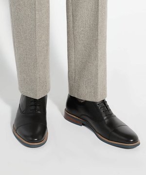 Chaussures habillées en cuir noir avec lacets portées avec un pantalon gris clair sur mesure sur fond blanc.