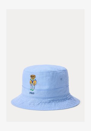 Gaiši zils spaiņa cepure no mīksta materiāla, ar izšūtu lāča dizainu, kurš tur dzērienu. Uz sāna izšūts "POLO" logo.