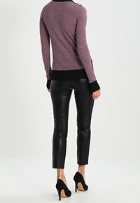 Gestreifter lila-schwarzer Pullover mit Rundhalsausschnitt, kombiniert mit glänzenden schwarzen Lederhosen und schwarzen hochhackigen Schuhen.