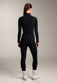 Fekete, hosszú ujjú felső és magas derekú leggings, fehér sportcipővel és világos rózsaszín bokazoknival párosítva. Sima textúra, testhezálló kialakítás.