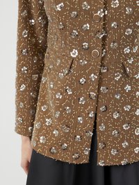 Veste en tissu marron avec des embellissements floraux en sequins, dotée d'une fermeture à boutons, de poches et d'une surface texturée.