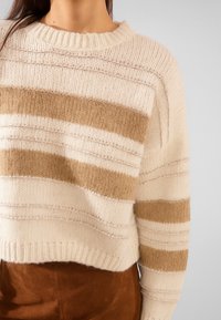 Pullover crema con strisce orizzontali beige e color sabbia. Presenta un collo a coste e un motivo di lavorazione a maglia strutturato. Design corto.
