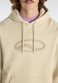 Felpa beige con cappuccio, caratterizzata da un logo ricamato in peluche sul petto, cappuccio regolabile con cordino e una tasca frontale. Tessuto morbido con una vestibilità comoda.