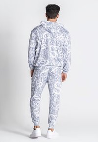 Tuta con cappuccio grigio chiaro con motivo a serpente. Il materiale sembra morbido, con polsini e vita elasticizzati, impreziosito da accenti bianchi.