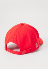 Red baseball cap with adjustable strap, embroidered white text reading "MIA SAN MIA" on the side, and a smooth fabric texture.