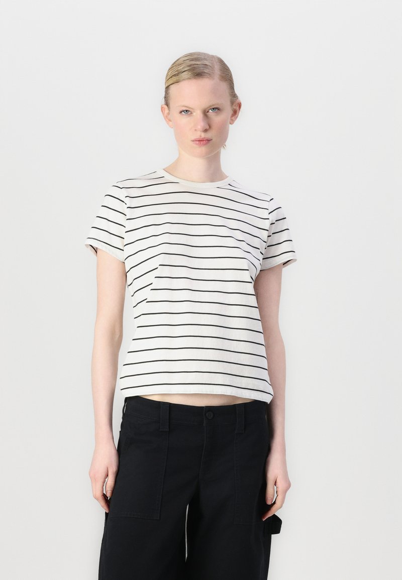 Striped t-shirt in light cream with thin black horizontal stripes, short sleeves, and a relaxed fit, paired with black cargo pants.