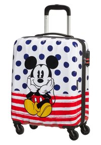 Valise rigide sur fond blanc, à pois bleu marine, bande rouge et graphique de Mickey Mouse. Comprend une poignée noire et quatre roues.