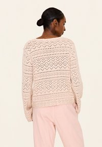 Helles rosa gestricktes Sweatshirt mit einem strukturierten, offenen Gewebe-Muster, das geometrische Designs aufweist. Lockerer Schnitt mit langen Ärmeln und einem gewellten Saum.