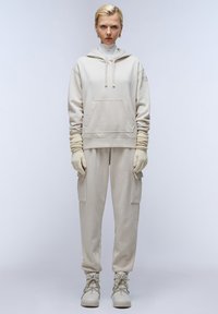 Beige hoodie met een voorzak, gecombineerd met bijpassende cargobroek en gebreide handschoenen. Kenmerkt zich door een gestructureerde stof en een ontspannen pasvorm.