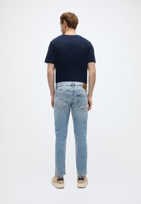 Μπλε ναυτικό κοντομάνικο μπλουζάκι συνδυασμένο με ανοιχτόχρωμο τζιν, με δερμάτινο ταμπελάκι στη ζώνη πίσω και μπεζ αθλητικά παπούτσια.