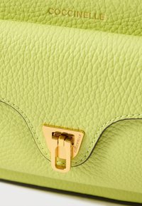 Grønn teksturert skinnhåndveske med gullfarget lås og preget logo. Buet design med kontrastfargede sømmer.