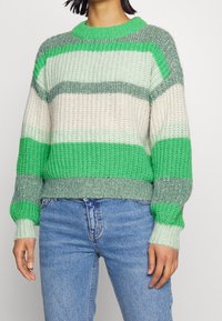 Sweter dzianinowy w poziome paski w kolorach zielonym, jasnoszonym i beżowym, z prążkowanym dekoltem i mankietami oraz luźnym krojem.
