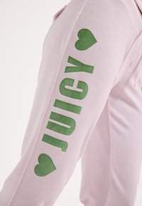 Rózsaszín szabadidőnadrág, oldalán nagy zöld "JUICY" felirattal és szív motívumokkal, puha, sima tapintású anyagból készült.