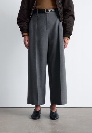 Gray wide-leg trousers with front pleats, made from textured fabric. Paired with a brown ribbed top and black flat shoes. Black belt with gold buckle.