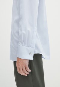 Himmelblaues Hemd mit langen Ärmeln und Manschetten, mit einem einzelnen Knopfverschluss. Glattes Material und sauberer Schnitt für einen maßgeschneiderten Look.