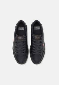 Baskets en cuir noir avec une texture lisse. Les caractéristiques incluent un bout rond, des perforations, des lacets gris et une étiquette de logo sur la languette.