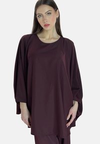 Bordeauxrote Tunika aus glattem Stoff, mit lockerem Schnitt, weiten Ärmeln und rundem Ausschnitt. Minimalistisches Design ohne Muster.