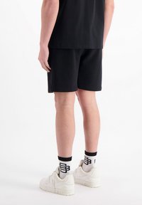 Zwarte katoenen shorts met een gladde textuur, zijzakken en een elastische tailleband. Draagt een paar witte sneakers en gemusterde sokken.