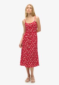 Rotes ärmelloses Kleid mit floralem Muster, tailliertem Oberteil und fließendem Rock in Midi-Länge. Träger und Knopfdetails sichtbar.