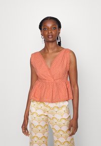 Top peplum cor pêssego com textura em ilhós, decote em V e bordas em forma de onda, combinado com calças largas estampadas em creme e dourado.