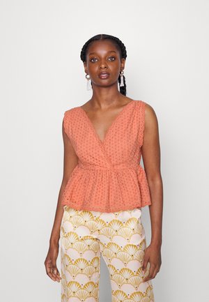Top peplum cor pêssego com textura em ilhós, decote em V e bordas em forma de onda, combinado com calças largas estampadas em creme e dourado.