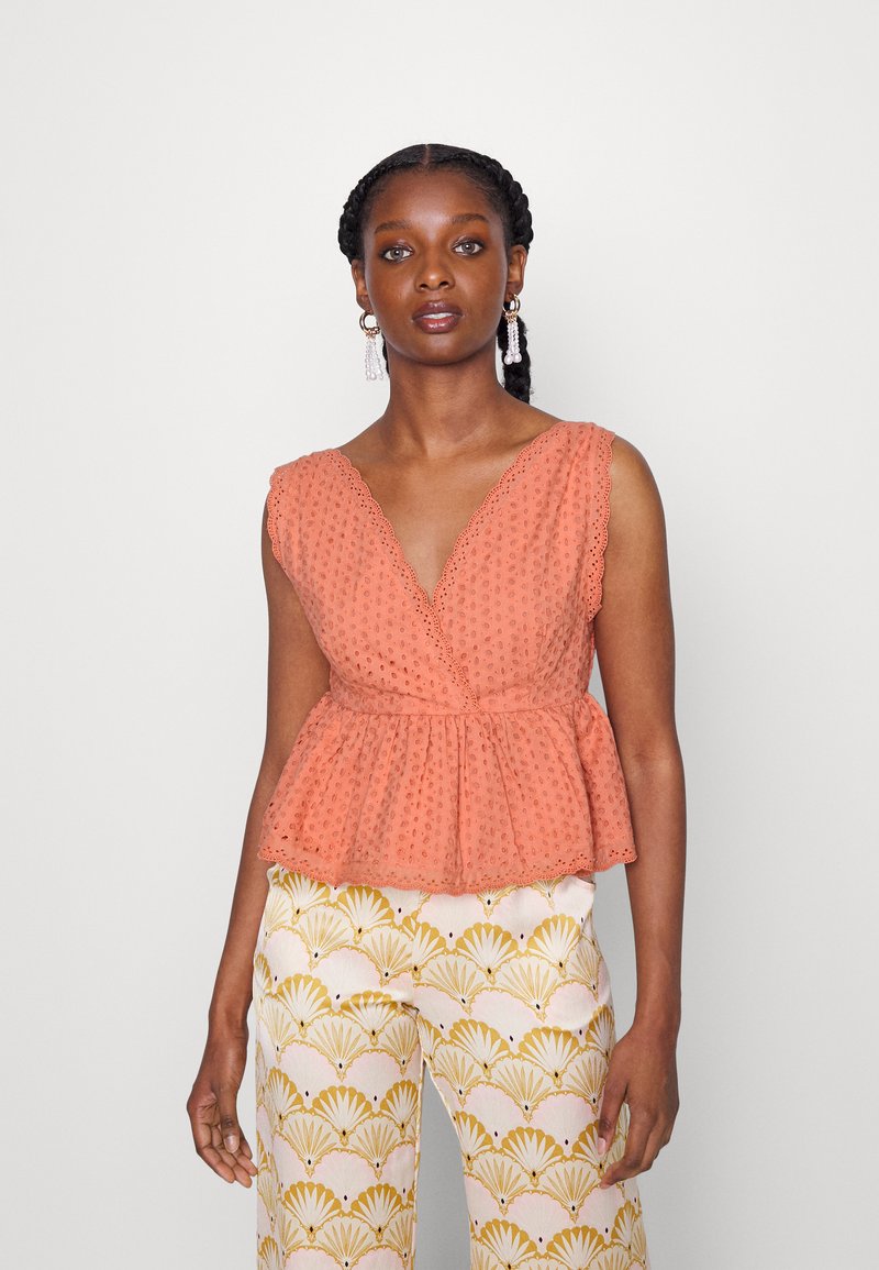 Top peplum cor pêssego com textura em ilhós, decote em V e bordas em forma de onda, combinado com calças largas estampadas em creme e dourado.