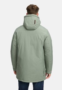 Parka verde isolato con cappuccio, texture liscia, taglio lungo e zip laterali. Presenta un'etichetta con logo sul retro.