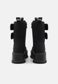 Botas negras hasta el tobillo hechas de cuero texturizado, con dos correas ajustables de velcro, un cierre de cremallera y una suela gruesa.