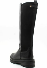 Botas negras hasta la rodilla, hechas de cuero liso y tela texturizada. Presentan una suela resistente, costuras mínimas y un pequeño acento cerca de la parte superior.