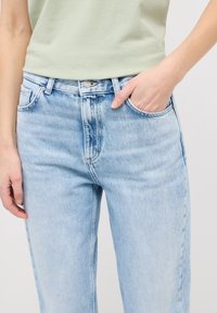 Jeans de tiro alto en azul claro y con un corte relajado. Fabricados en denim, cuentan con un cierre frontal con botón, cinturilla y bolsillos laterales. Textura suave.