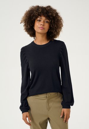 Pull en navy avec des manches longues et bouffantes, finitions en côtes. Texture douce et col rond. Associé à un pantalon beige.