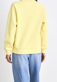 Felpa gialla con collo a barca, maniche raglan e polsini a coste. Abbinata a jeans in denim blu chiaro, con una vestibilità rilassata.