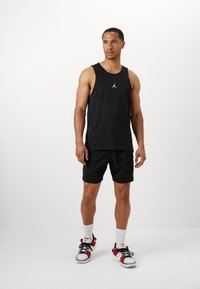 Débardeur de sport noir avec le logo Jordan, associé à un short noir. Porté avec des chaussettes de cheville blanches et des baskets multicolores. Design simple.