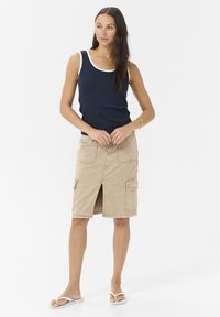 Débardeur marine avec une bordure blanche, associé à une jupe cargo beige avec des poches et une fente avant. Porté avec des claquettes blanches.