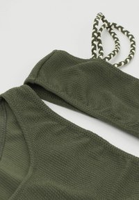 Olivově zelený texturovaný plavkový top s tkaným popruhem. Disponuje měkkou, žebrovanou tkaninou a trojúhelníkovým designem. Mezi akcenty je také pletená šňůrka.