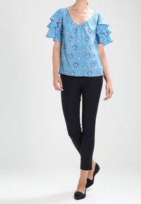 Blå blommönstrad blus med korta volangärmar, V-ringning, i kombination med svarta slim fit-byxor och svarta ballerinas.