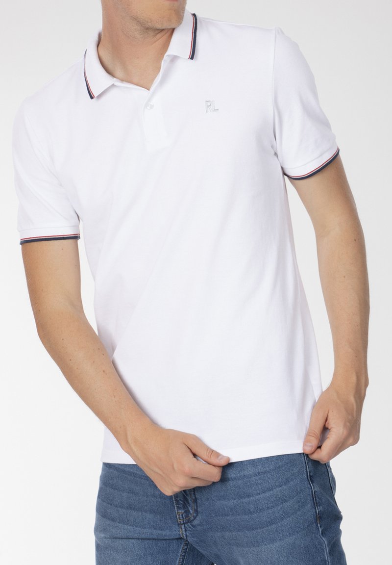 Polo blanc avec un plastron à deux boutons, logo brodé et empiècements contrastants rouges et bleus sur le col et les manches.